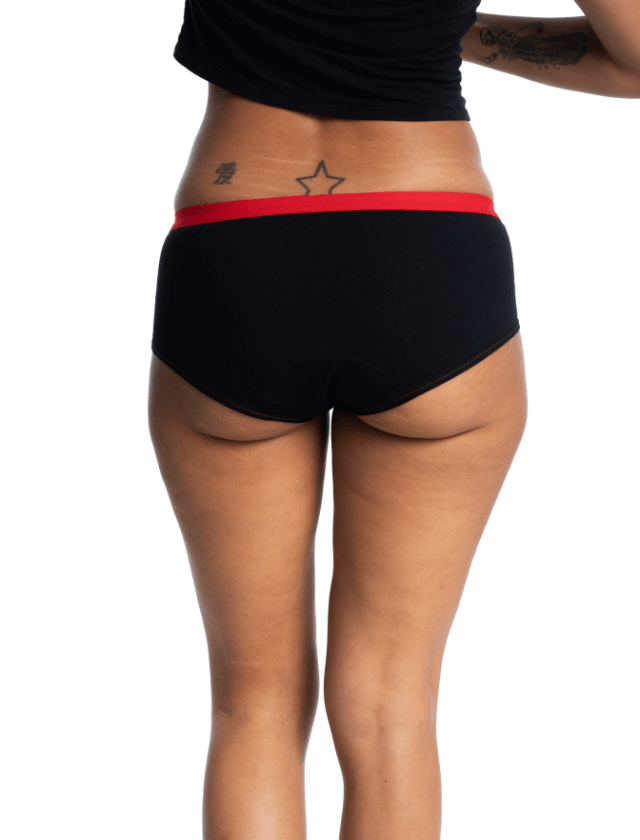 Shorty menstruel de la marque Mme L’ovary, noir et élastique rouge. Flux léger sans le pad, abondant avec le pad. Ce modèle est vendu avec une pochette à deux compartiments et 3 pads amovibles. Tailles du XXS au XXL. A retrouver dans les boutiques menstruelles Rañute, en Suisse.