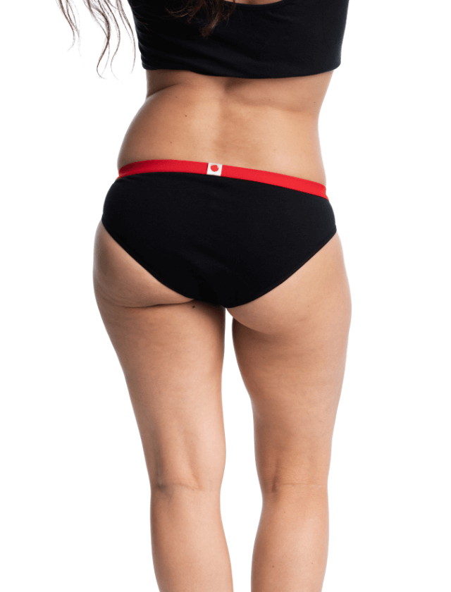 Culotte menstruelle bikini noire avec élastique rouge, vendues avec trois serviettes amovibles pour flux légers à flux abondants. Vue de derrière